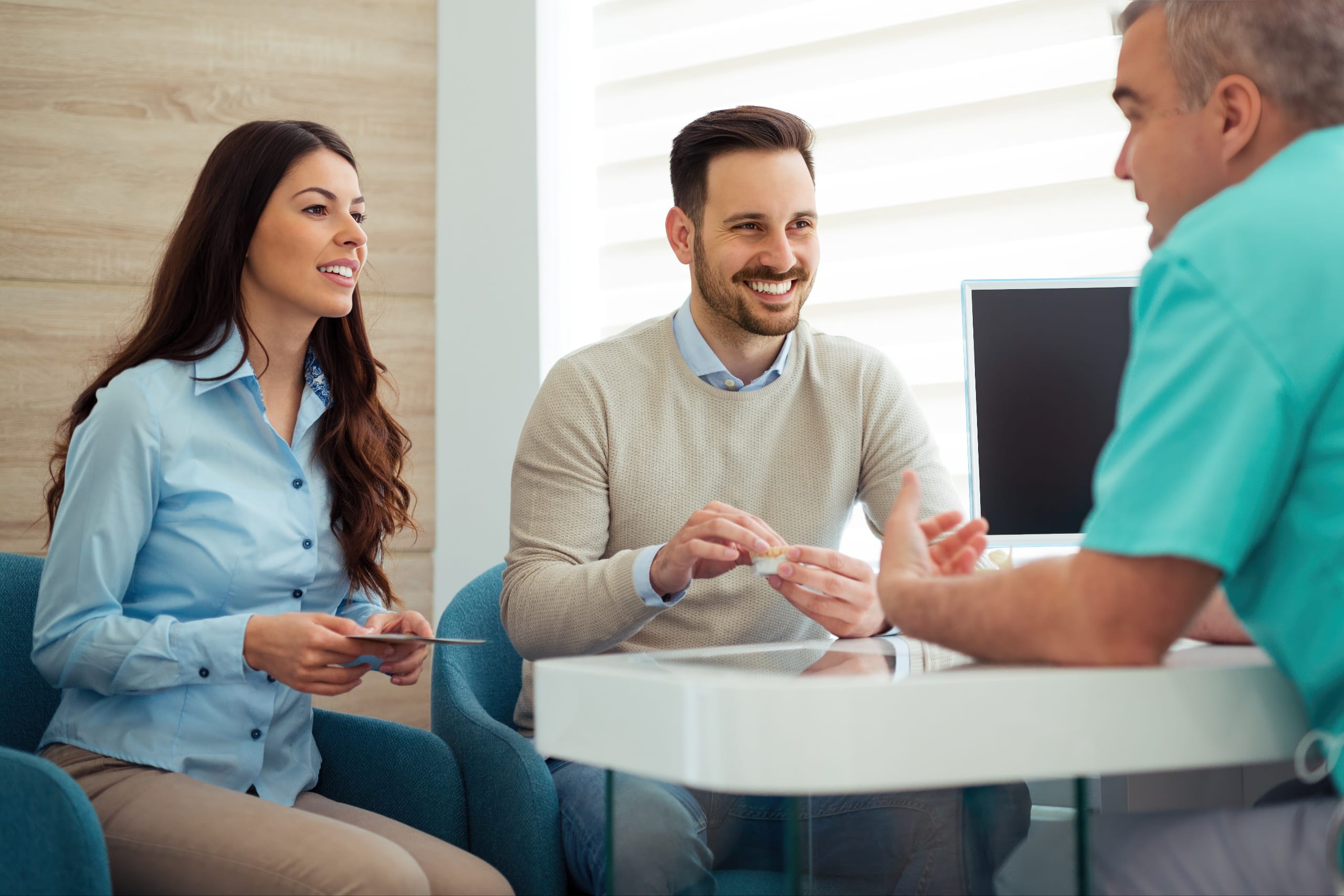 Smiling couple sitting across from a dental professional during a consultation, discussing treatment options and financing in a modern office setting.