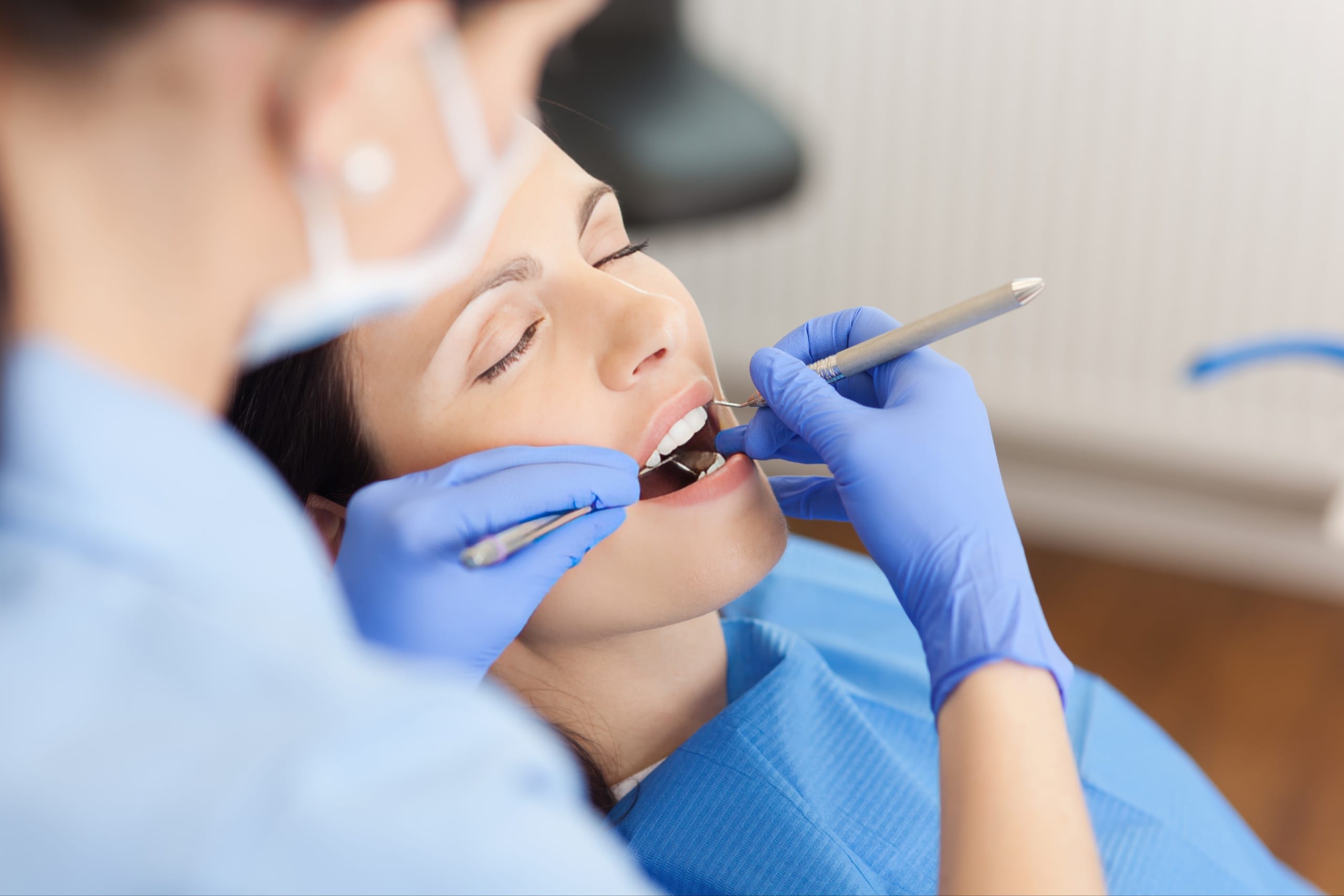 Female patient receiving dental treatment with her eyes closed, while a dental professional uses tools in her mouth—representing sedation dentistry for a relaxed and anxiety-free dental experience.