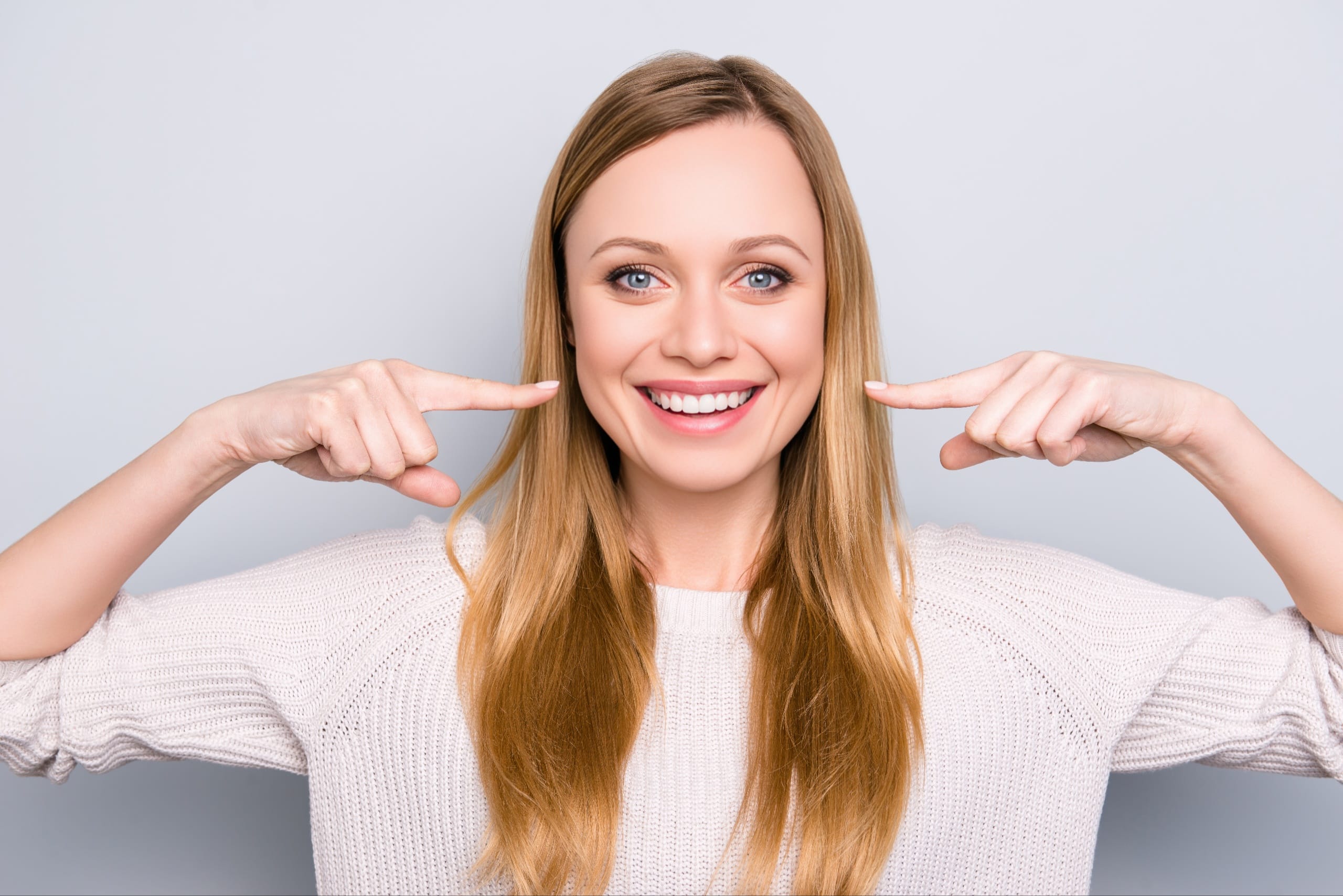 Smiling woman pointing to her bright white teeth, expressing satisfaction—ideal for a dental testimonial or success story.