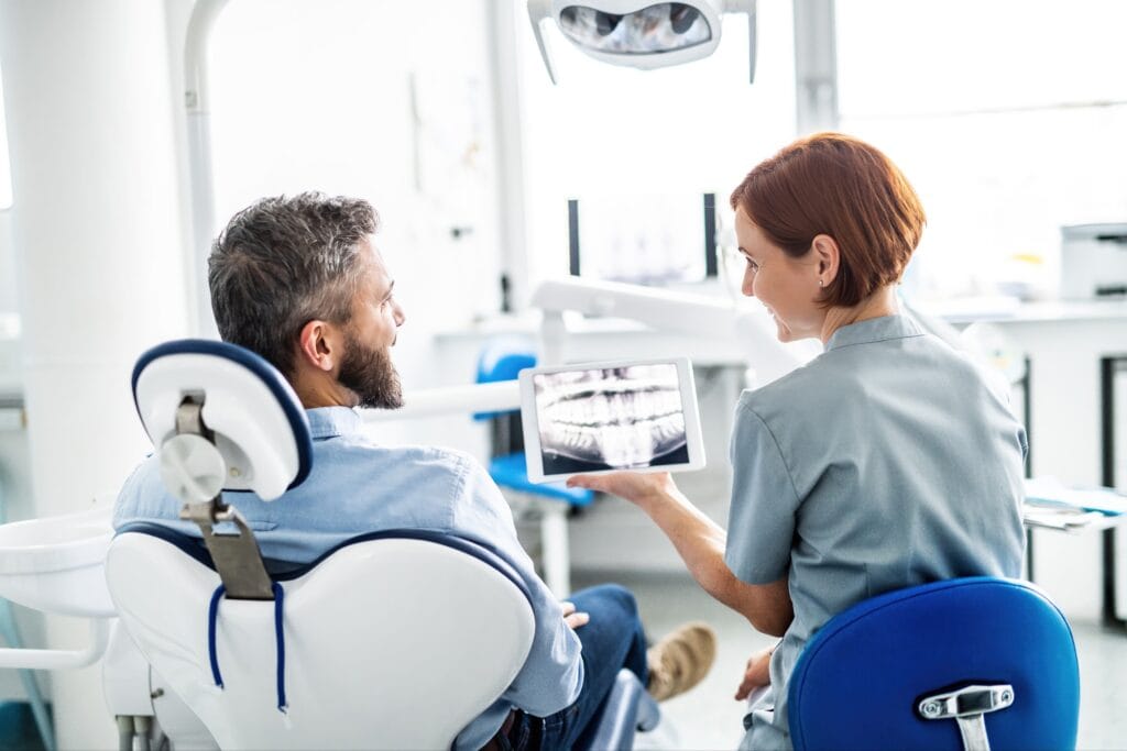 Dental professional showing a male patient his dental X-ray on a tablet during a consultation in a modern dental clinic.