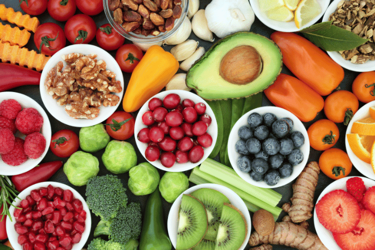 A colorful overhead display of fresh fruits, vegetables, nuts, and herbs arranged in bowls and scattered on a surface.