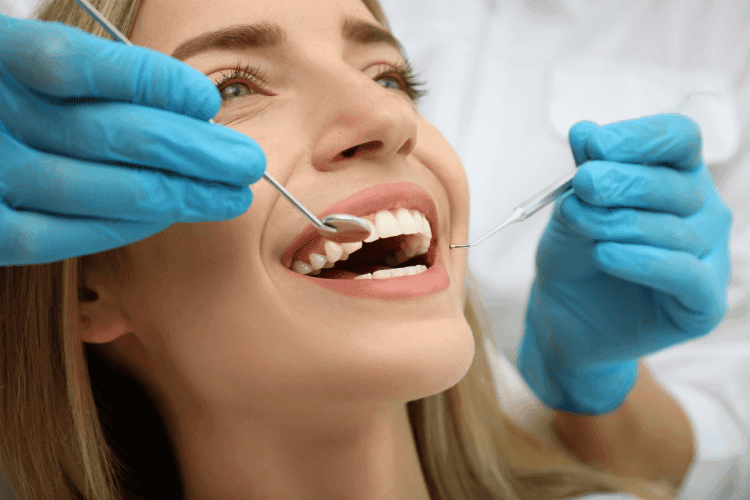 A woman smiling while a dentist uses dental instruments to examine her teeth.