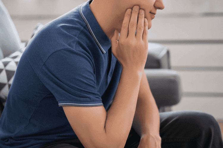 Man experiencing jaw pain while sitting at home.
