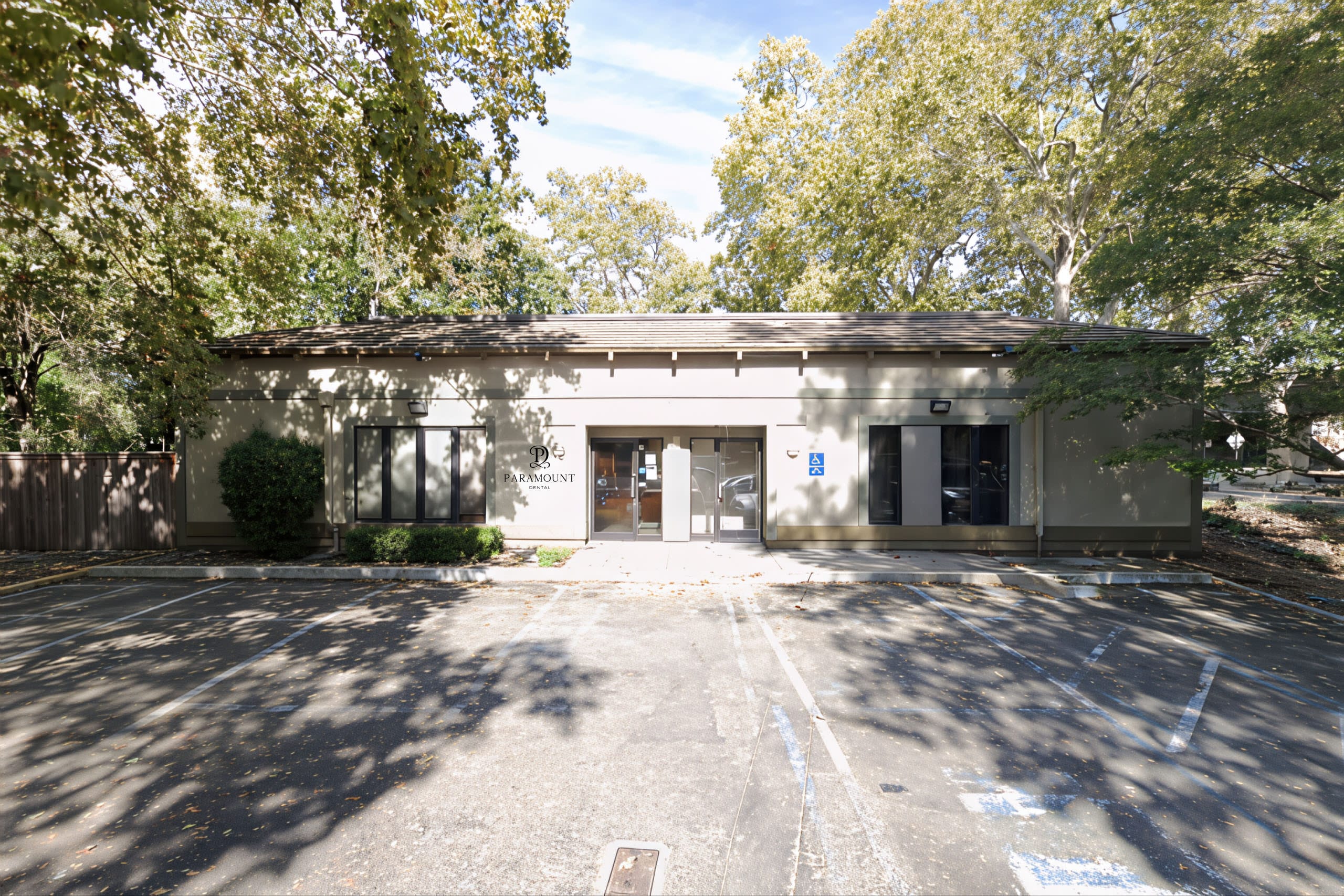 Single-story dental office building with Paramount Dental signage, glass entry doors, and shaded parking spaces in front.