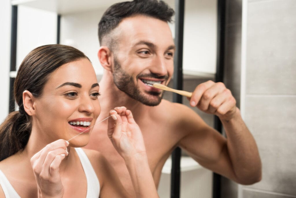 Couple practicing preventive dental care by brushing and flossing together in a modern bathroom mirror. Daily preventive